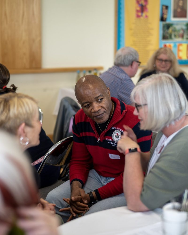 Divine Renovation event. A middle-aged man in a parish, listening intently as others from his prayer group share their reflections.